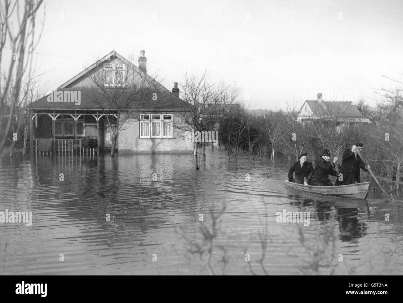 A policeman and rescue worker row a flood victim from her home at Canvey Island, Essex. Stock Photo