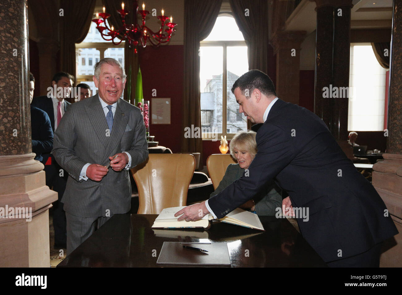 The Prince of Wales (left) laughs as The Duchess of Cornwall signs the visitors' book as the General Manager Kevin Kelly (right) looks on during a visit to the recently regenerated St Pancras Renaissance London Hotel adjacent to St Pancras International Station in London as they mark 150 years of London Underground. Stock Photo