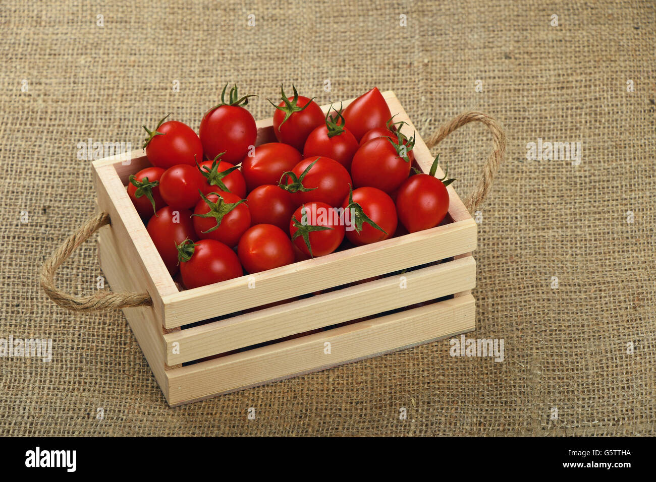 Red ripe fresh cherry tomatoes in small wooden box with twine jute