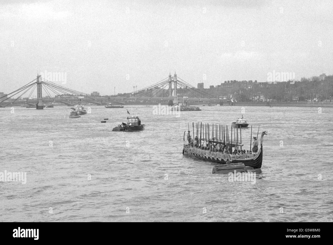 Rare Victorian elegance, the Albert suspension bridge and second oldest surviving bridge in London, forms the background for today's friendly invasion by a troop of Danish Boy Scouts. They are sailing up the River Thames to Battersea Park in a IMME GRAM (foreground), a 71-foot full-scale replica of a Viking longship, which they built under the direction of their scoutmaster, Mr T. Harvig Nielsen. The scouts rowed the vessel up the Thames from Tower Pier to Battersea Pier for the inaugural luncheon of the 'At Home With The Danes' exhibition. The last time a Viking longship came up London's Stock Photo