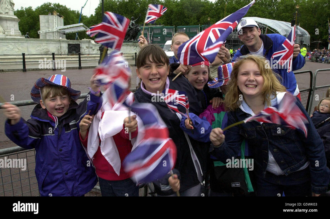 Children wave their Union Jack flags outside Buckingham Palace. Britain's Queen Elizabeth II and the Duke of Edinburgh will leave Buckingham Palace in a Gold State Coach for a thanksgiving service at St Paul's Cathedral. * .... before returning to watch a parade in The Mall on the final day of the Golden Jubilee Bank Holiday weekend. Stock Photo