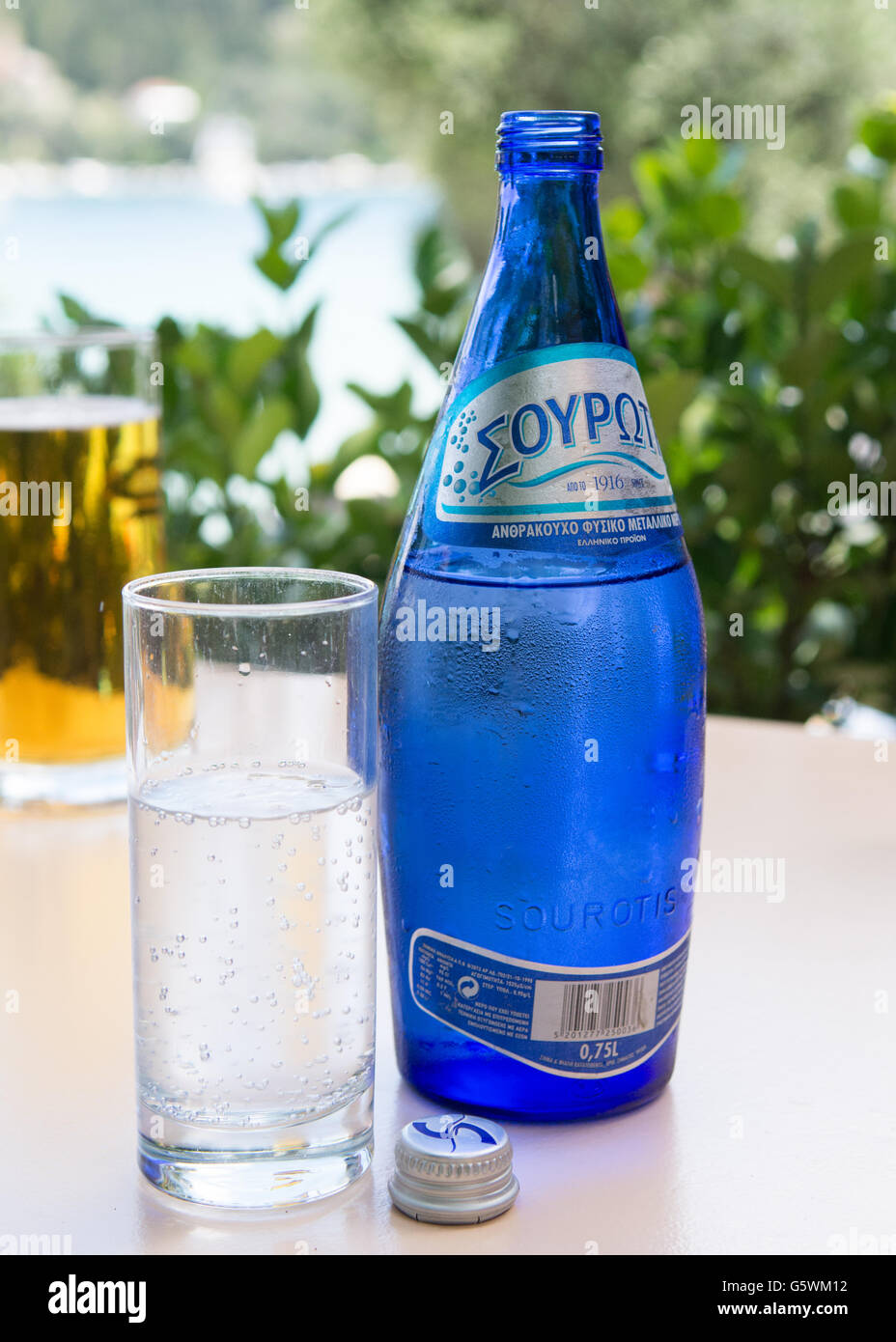 chilled bottle of water on taverna table on greek island with glass of chilled beer and sea in the background Stock Photo