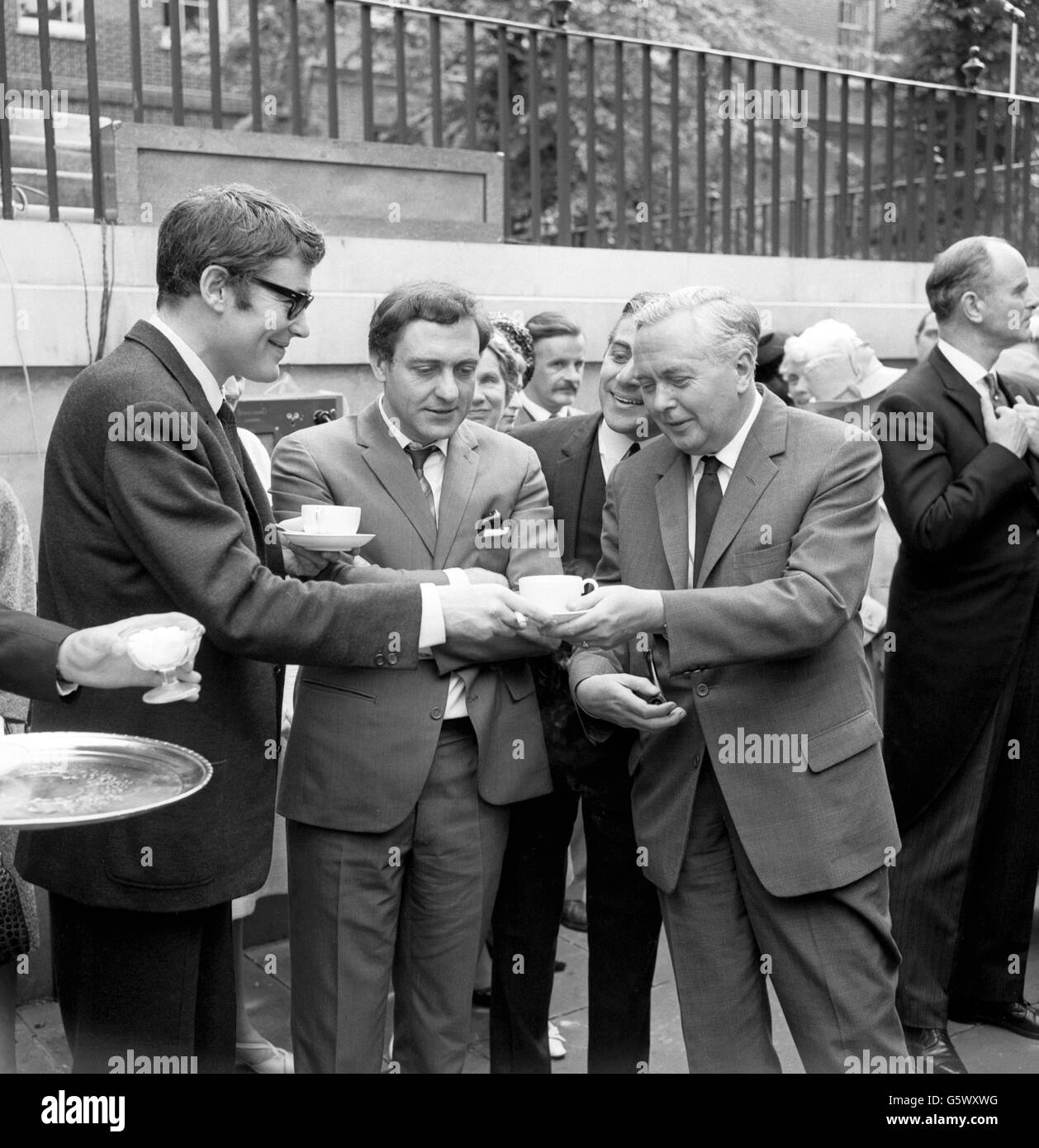 Film star Peter O'Toole hands Prime Minister Harold Wilson a cup of tea at the United Nations Association's (UNA) garden party held at 10 Downing Street, London. In the centre of the picture is Steptoe and Son actor Harry H. Corbett. The garden party was held to raise funds for the Association's work and guests included members of the Diplomatic Corps and prominent people in the Entertainment world. The UNA was founded in 1945 to support and strengthen the United Nations through education, influence and practical activities. Stock Photo