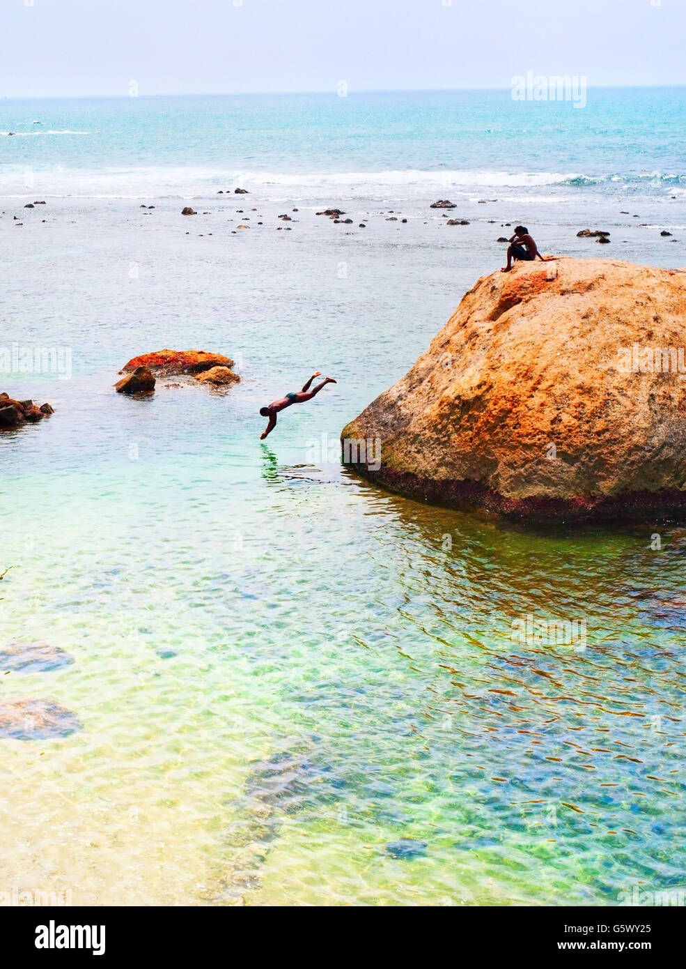 Boys swimming and jumping to the ocean from the rock. Sri Lanka Stock Photo
