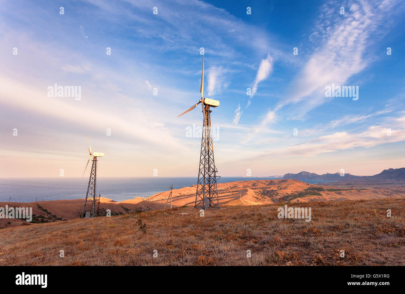 Industrial landscape with wind turbine generating electricity in mountains at sunset. Stock Photo