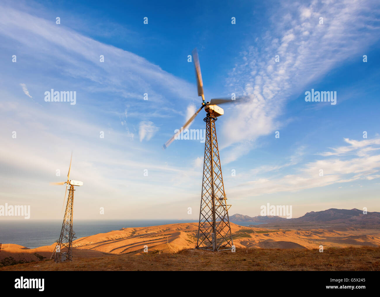 Industrial landscape with wind turbine generating electricity in mountains at sunset. Stock Photo