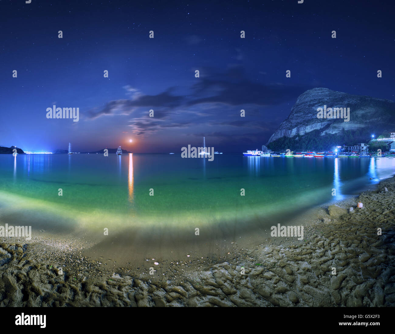 Beautiful night landscape at the seashore with yellow sand, full moon, mountains and lunar path. Moonrise. Panoramic view. Stock Photo