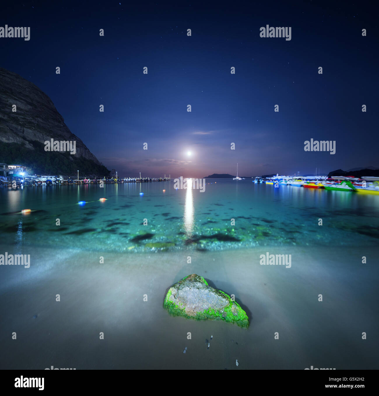 Beautiful night landscape at the seashore with yellow sand, full moon, mountains and lunar path. Moonrise. Panoramic view. Stock Photo