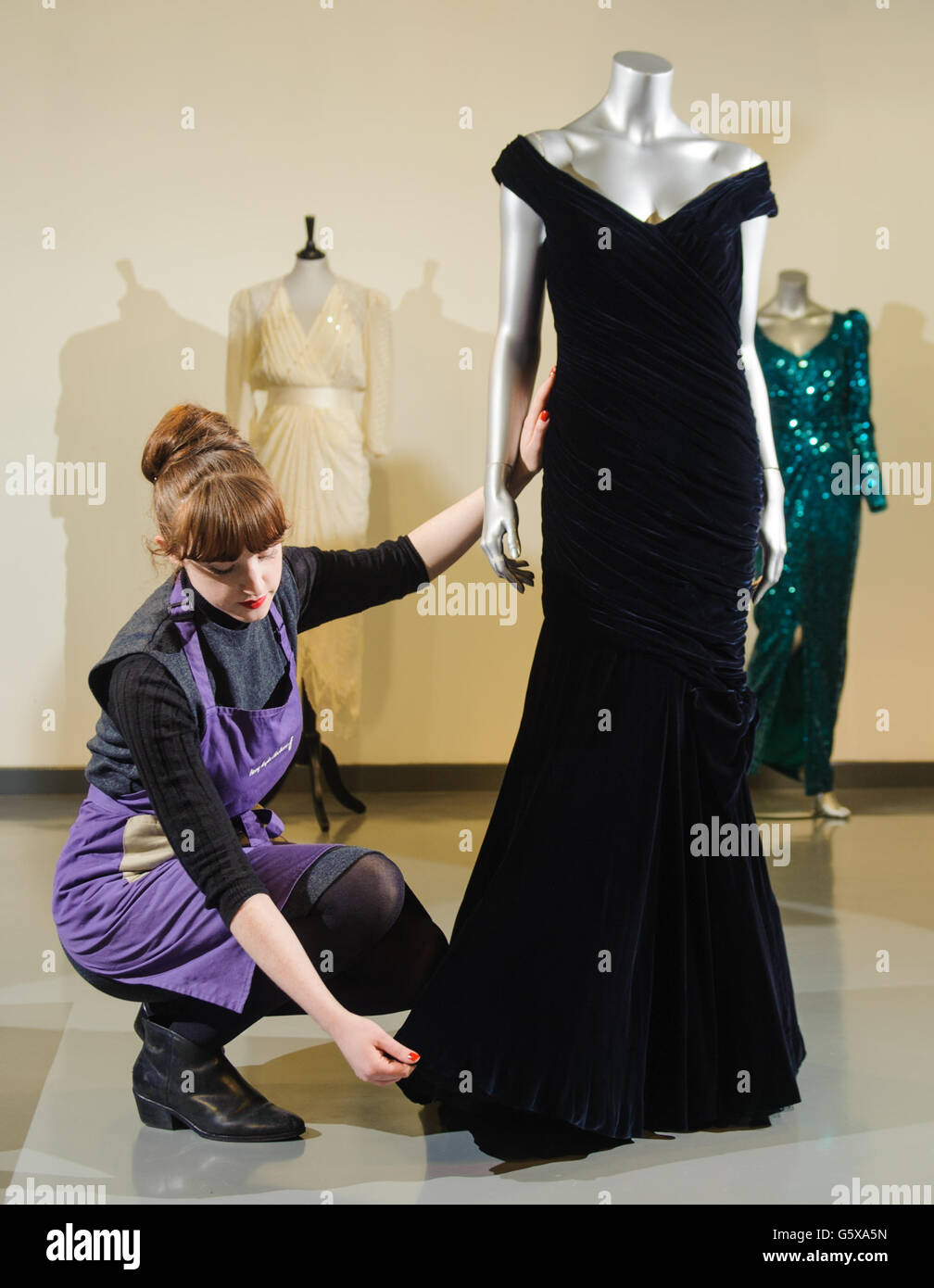 House assistant Lucy Bishop adjusts a midnight-blue velvet Victor Edelstein evening gown, at Kerry Taylor Auctions, in central London, the gown formerly owned by Princess Diana, which she wore when she danced at the White House with John Travolta in 1985. Stock Photo