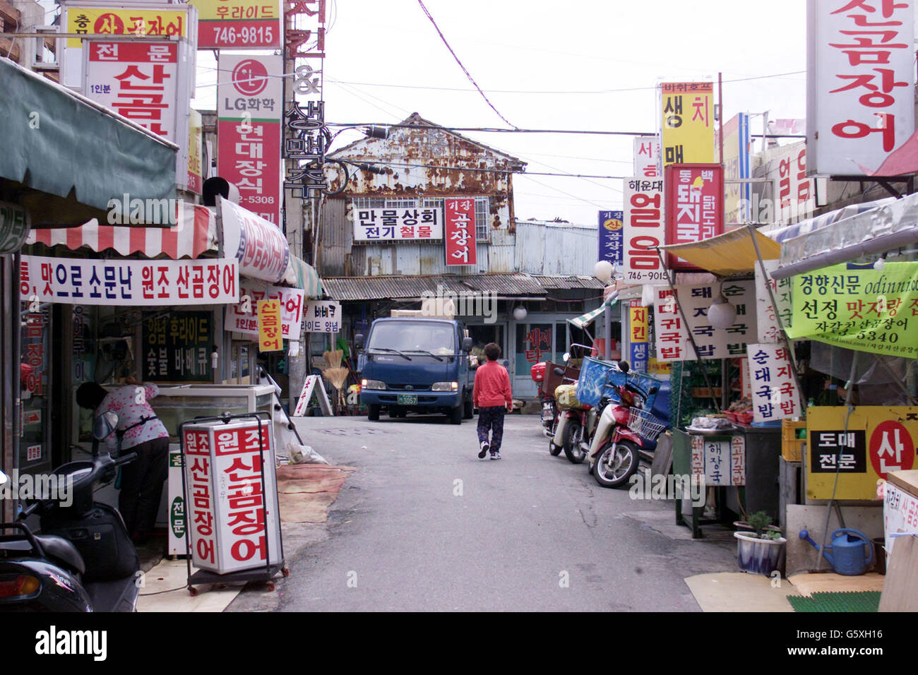 Small shops and market stalls line this street in Busan where the buildings are covered in various signs and adverts. Stock Photo