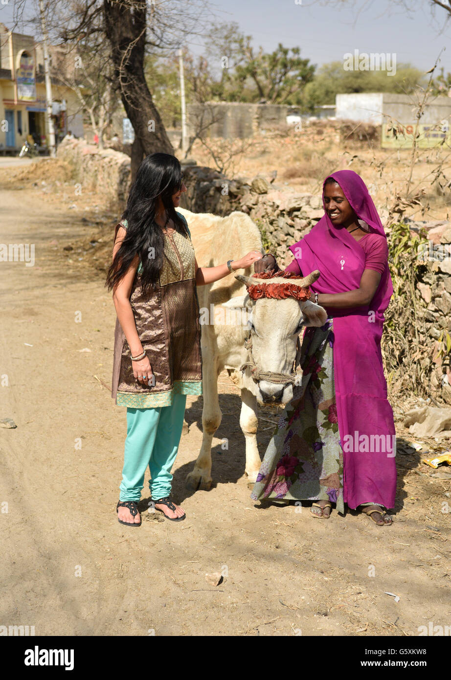 Beautiful urban woman in light Indian pyjama dress with long black hair expressing emotional farewell to her rural friend in sari outside her village. Stock Photo