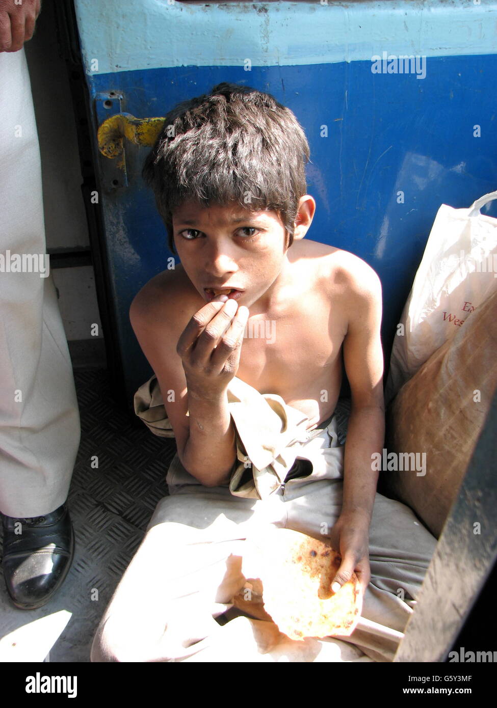 A poor hungry boy eating a stale roti (bread) in an Indian train Stock Photo
