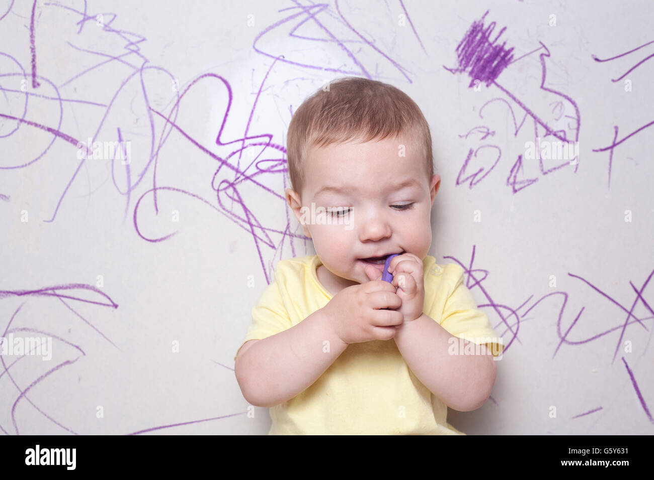 Baby boy drawing with wax crayon on plasterboard wall. He has the