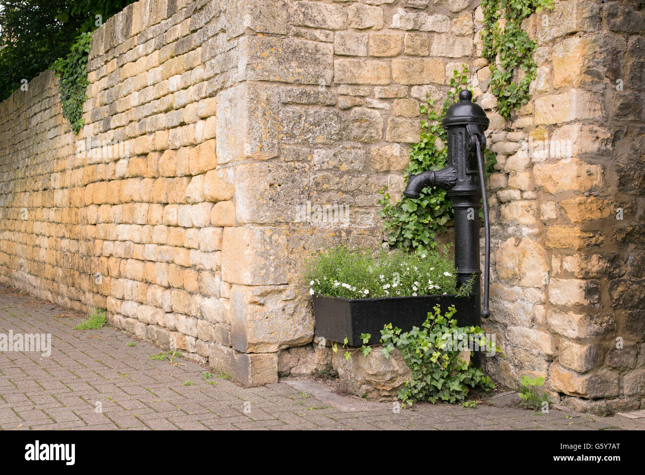 Old cast iron hand water pump and trough with flowers on the street in in Chipping Campden, Gloucestershire, England Stock Photo
