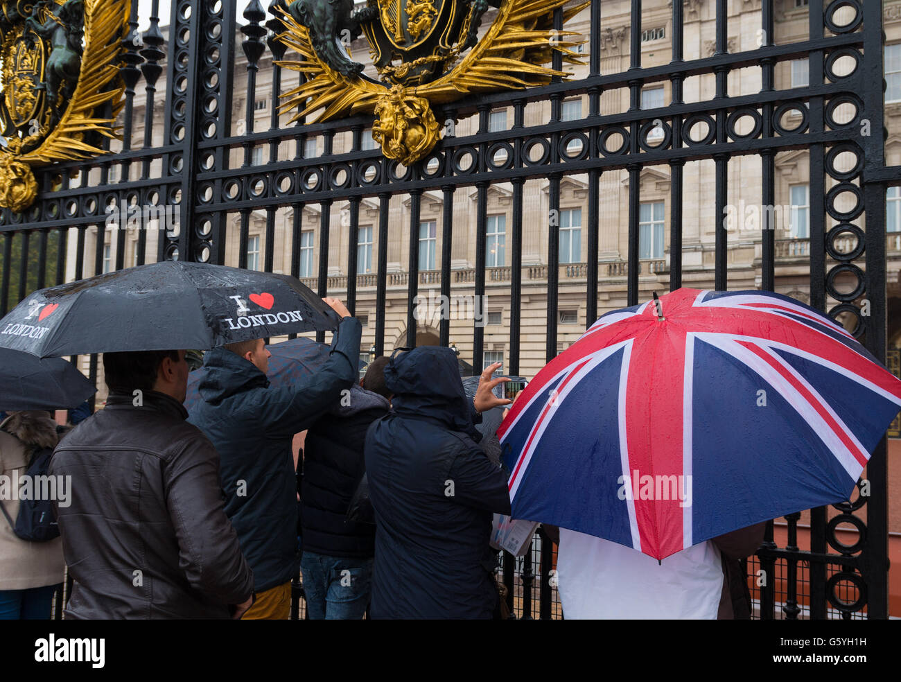 LONDON, ENGLAND - OCTOBER 21, 2015: Tourists looking through a gate of Buckingham palace on a rainy day. Buckingham palace is th Stock Photo