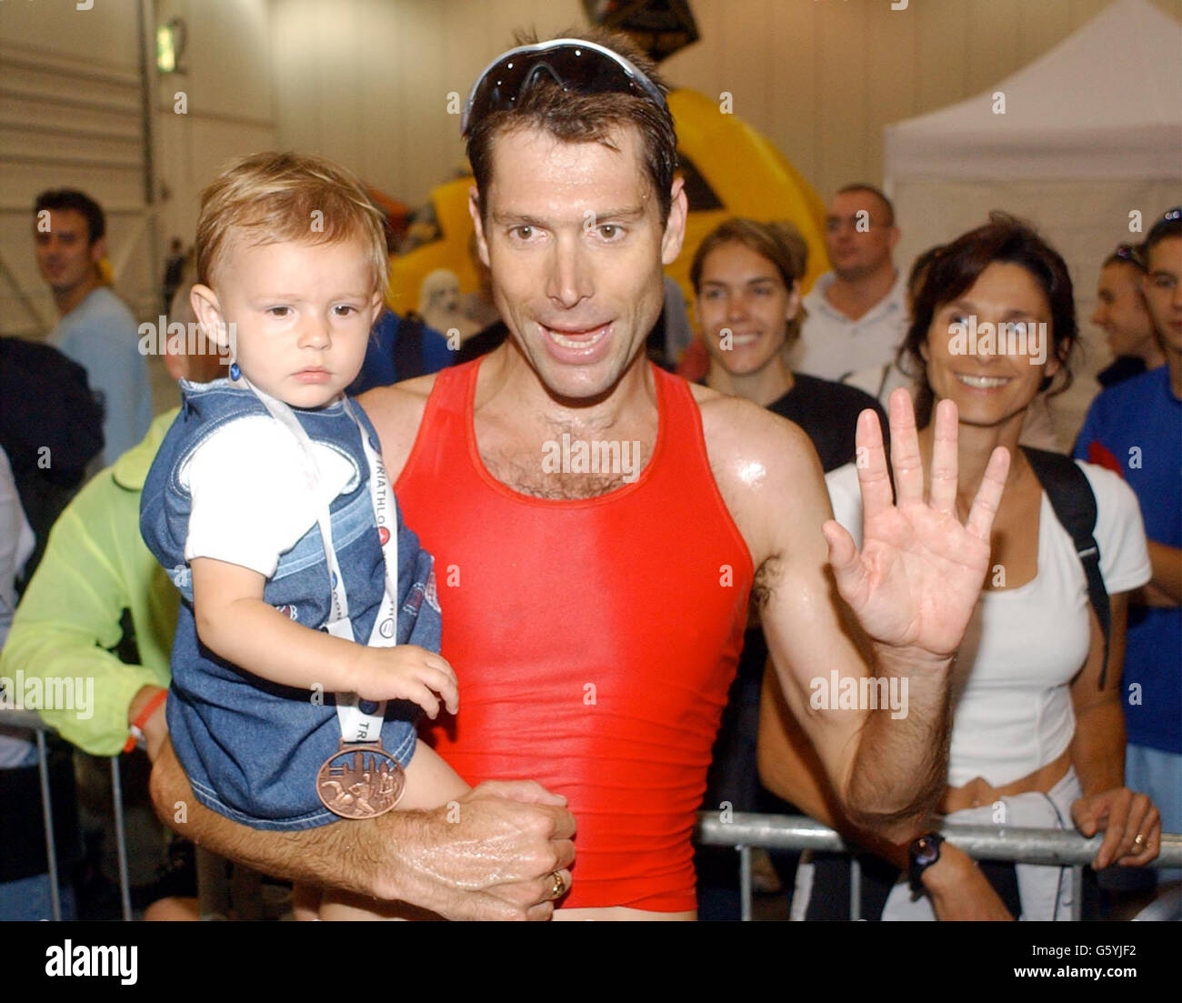 Mens Elite champion Simon Lessing of England and his baby wave to fans while his wife (right behind) looks on during the London Triathlon at Royal Victoria Docks. Stock Photo