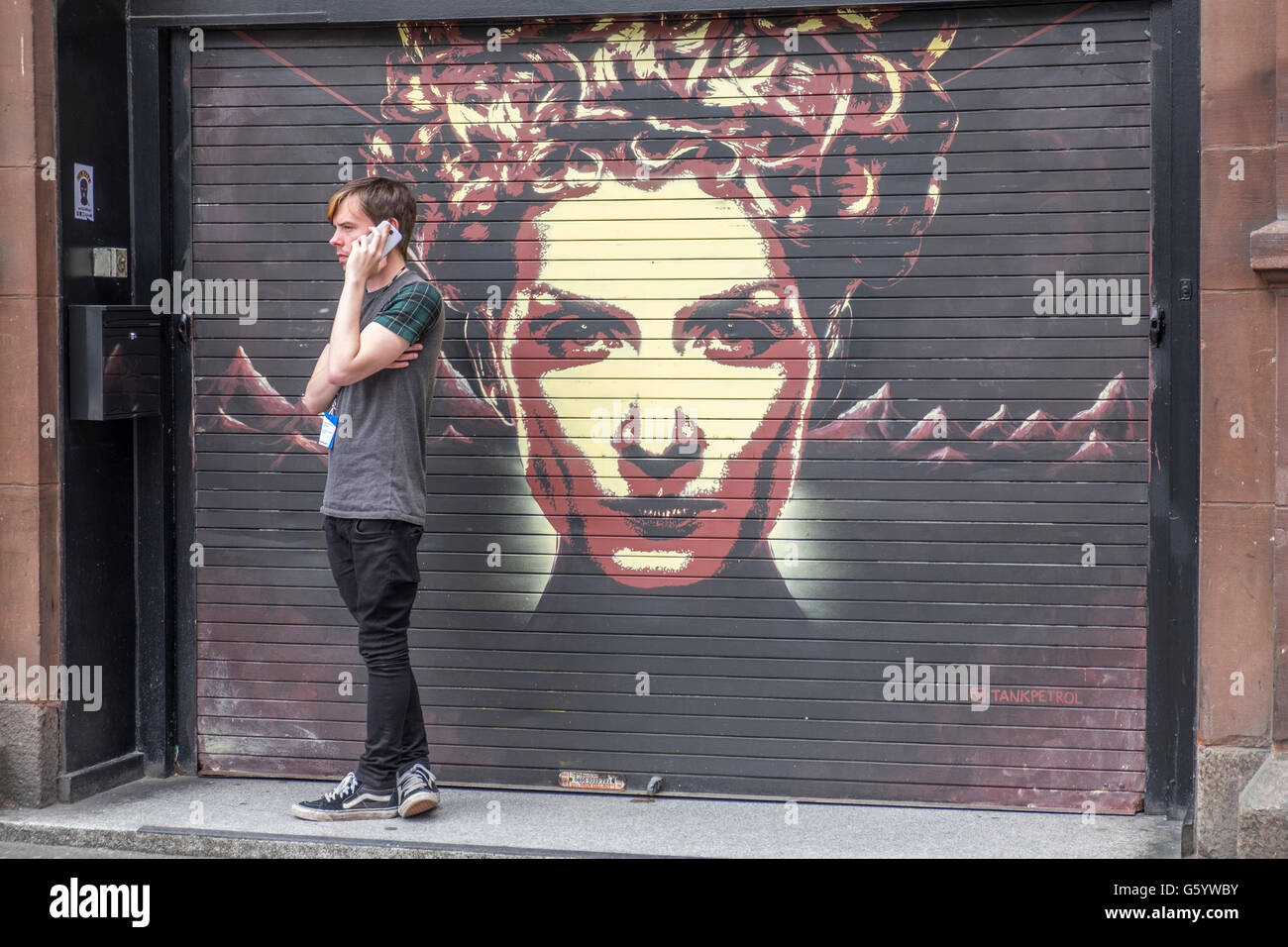 A man stood in a doorway whilst speaking on a mobile phone with a wall art painting of a lady behind him. Stock Photo