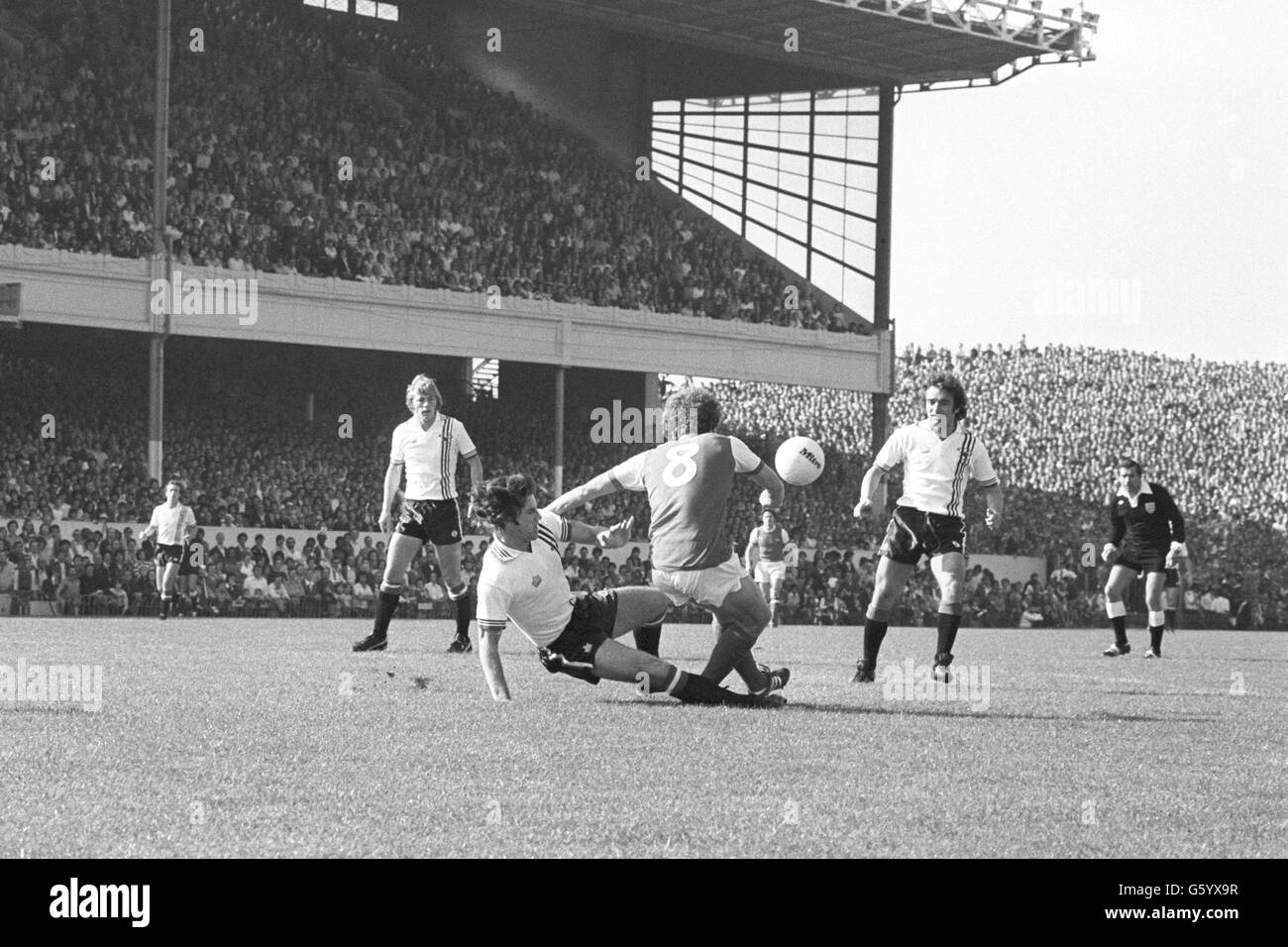 Martin Buchan of Manchester United slides in to tackle Arsenal's Alan Sunderland during a League One match at Highbury. Looking on are Manchester United players Brian Greenhoff (left) and Lou Macari. Stock Photo