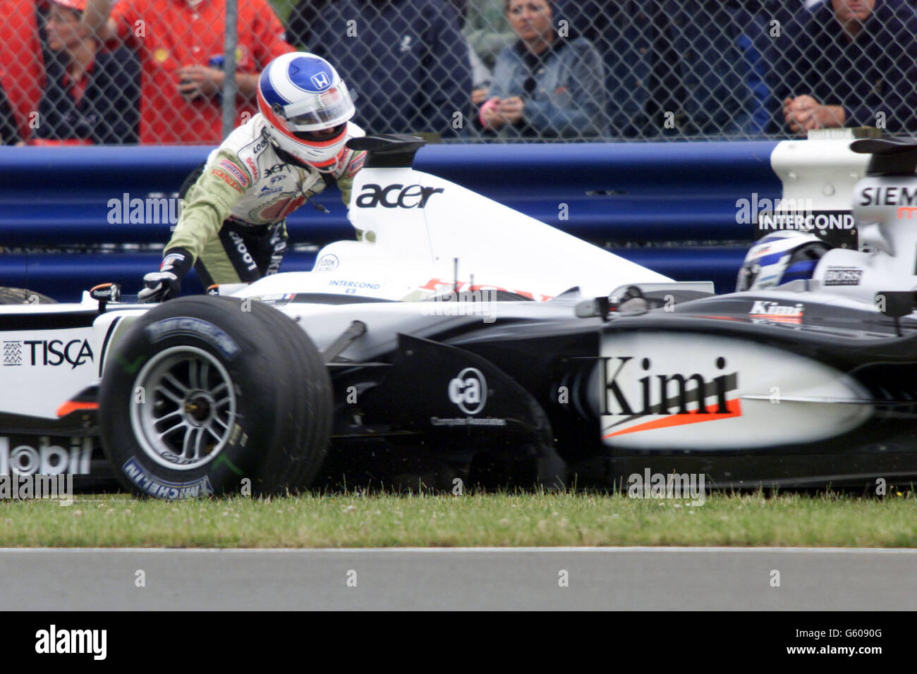 As David Coulthard in a McLaren comes onto the curcuit Lucky Strike BAR driver Olivier Panis stalls his car and has to push his car about 300 yards back to the pit lane before he can restart the engine and take his place on the grid before the start of the British Grand Prix. Stock Photo