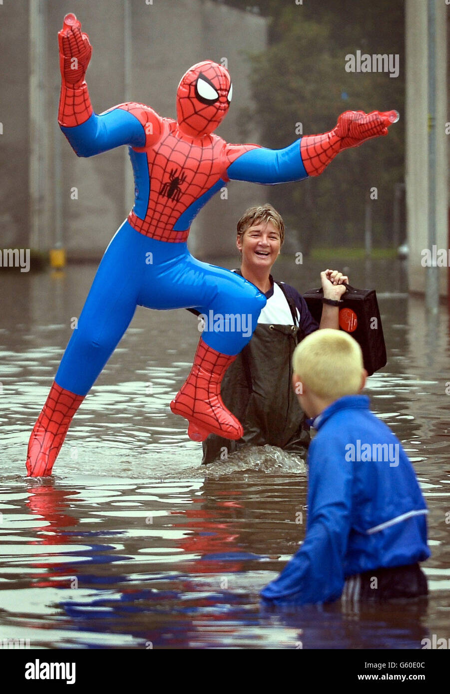 Resident Ally Allan cannot help but laugh as she carries an inflatable  Spiderman figure, one of her many drenched possessions, from her flooded  flat across the street to a neighbour's to dry