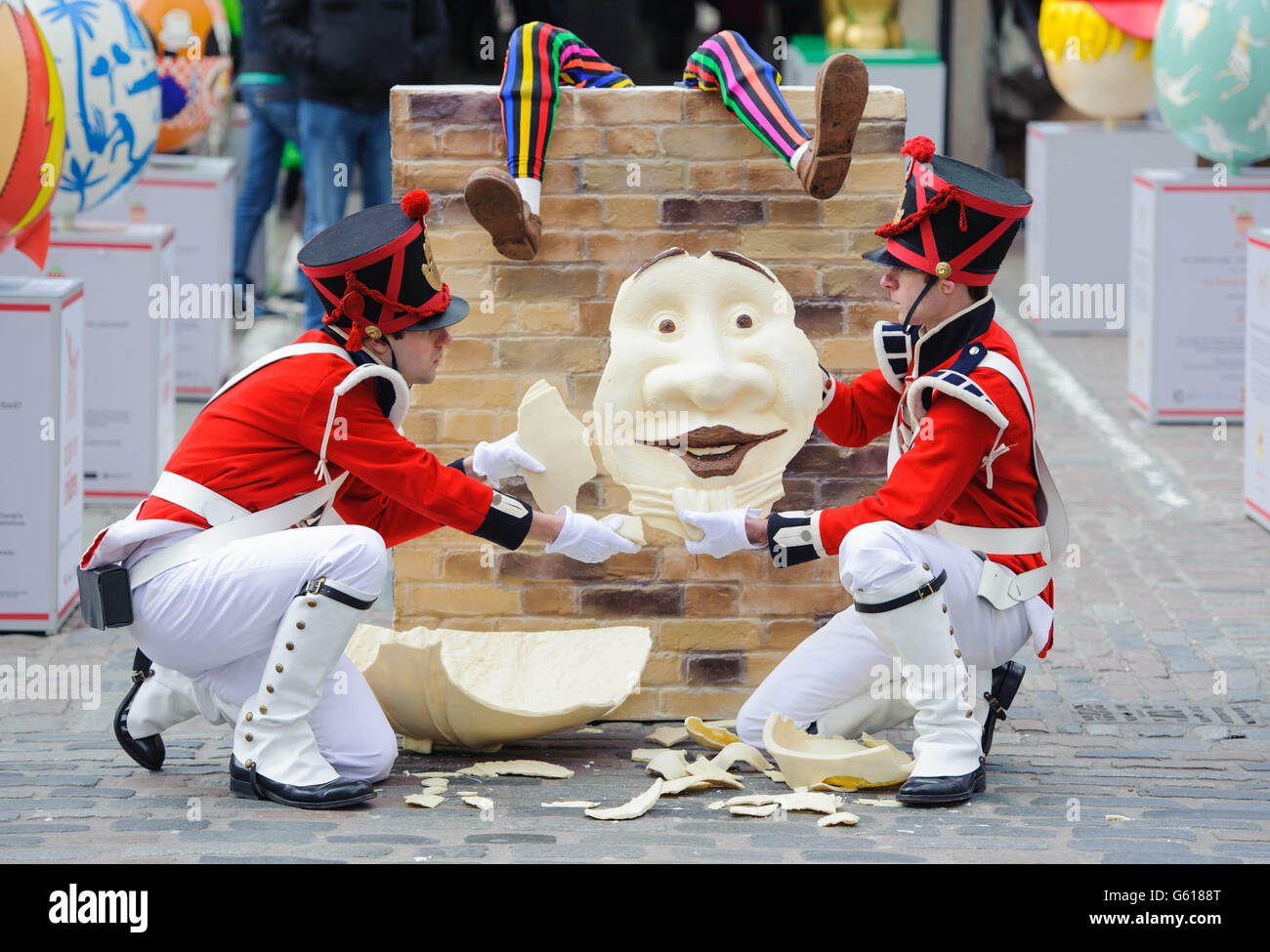 Christian Ward (left) and Kevin Kemp dressed as soldiers examine the remains of a shattered 4ft tall Humpty Dumpty style Easter egg in Covent Garden, central London, as part of the Lindt Big Egg Hunt supporting children's charity Action for Children. Stock Photo