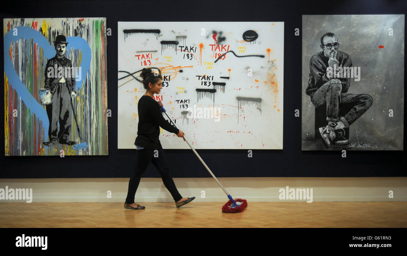 Mr Brainwash's Chaplain 2011 (left) Taki's Untitled 2009 (centre) and Jef Aerosol's Keith Haring 2012 (right) are displayed as gallery assistant Jacqueline Sevcik sweeps the floor during the preview for Climbing The Walls With Banksy at Bonham's Urban Art Sale at Bonham's auction house, London. Stock Photo