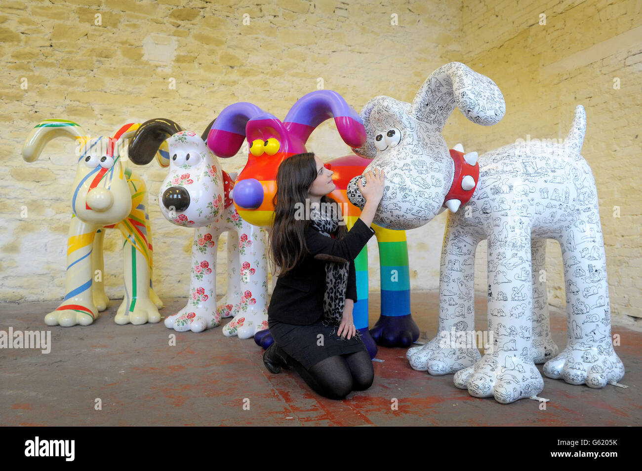 Lauren Vincent, fundraising manager for Gromit Unleashed, poses with four, of around 70, Gromit sculptures painted by (left to right) Sir Paul Smith, Cath Kidston, Richard Williams and Simon Tofield, at a secret location in Bristol before they are placed for public view on an arts trail around the city from July 1st. After the public arts trail the sculptures will be auctioned to raise funds for Wallace and Gromit's Grand Appeal's campaign to raise funds for the expansion of Bristol Children's Hospital. Stock Photo