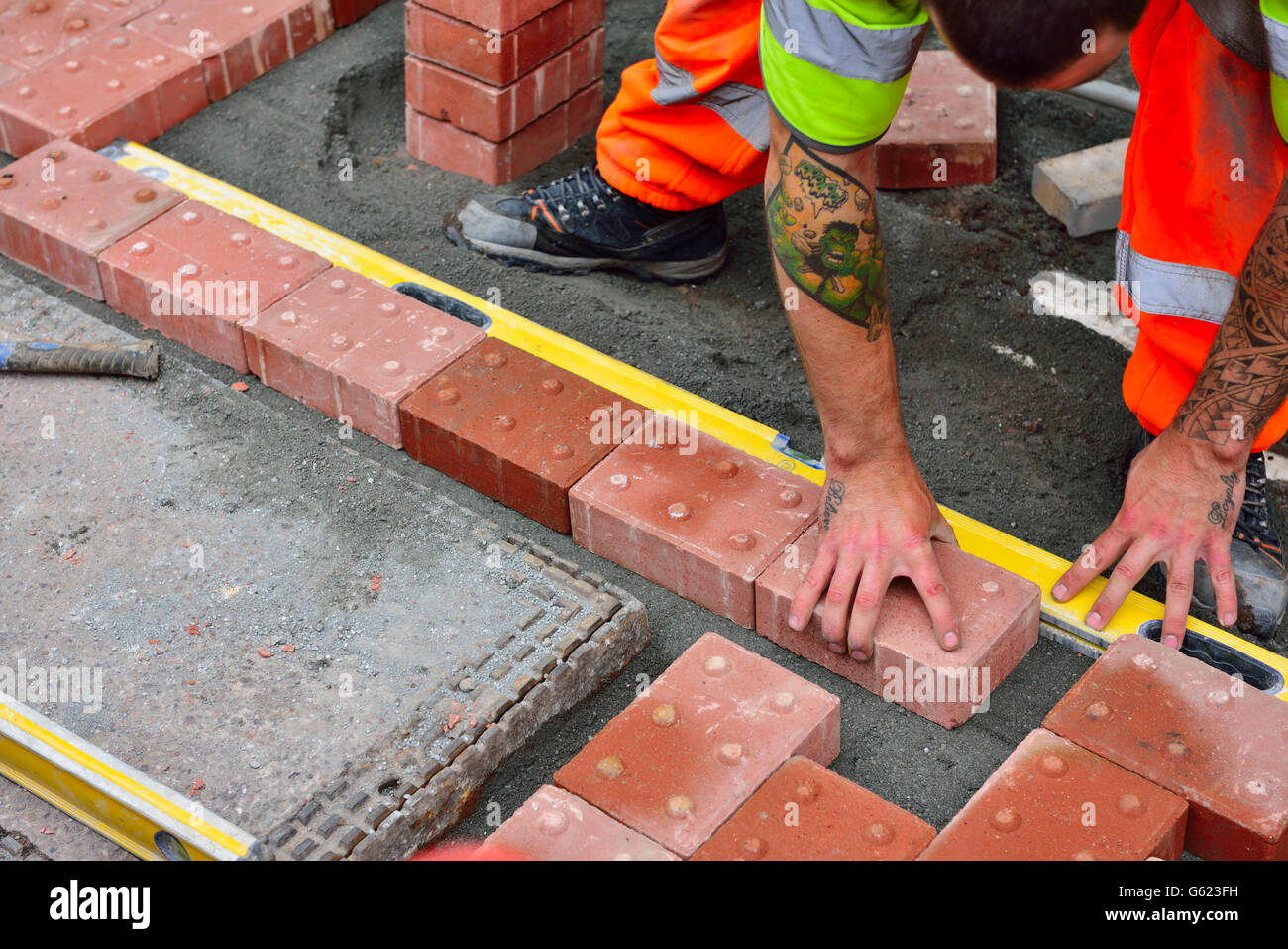 Workman laying tactile paving in footpath to assist visually impaired Stock Photo