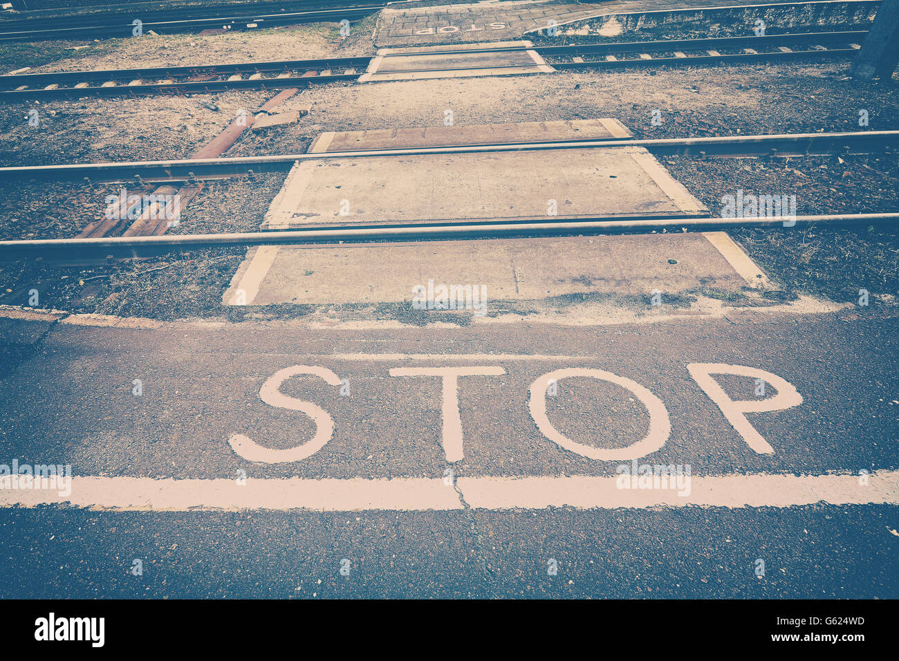 Vintage toned stop sign painted in front of railroad tracks. Stock Photo