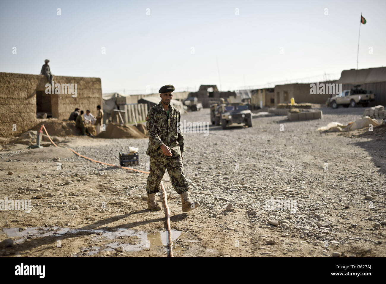 An Afghan National Army soldier strolls past Afghan construction work at Patrol Base Clifton, now renamed PB Oqab, as it houses only Afghan National Army soldiers and is being built to suit their specific needs as ISAF forces begin to handover bases and leave Afghanistan in 2014. Stock Photo