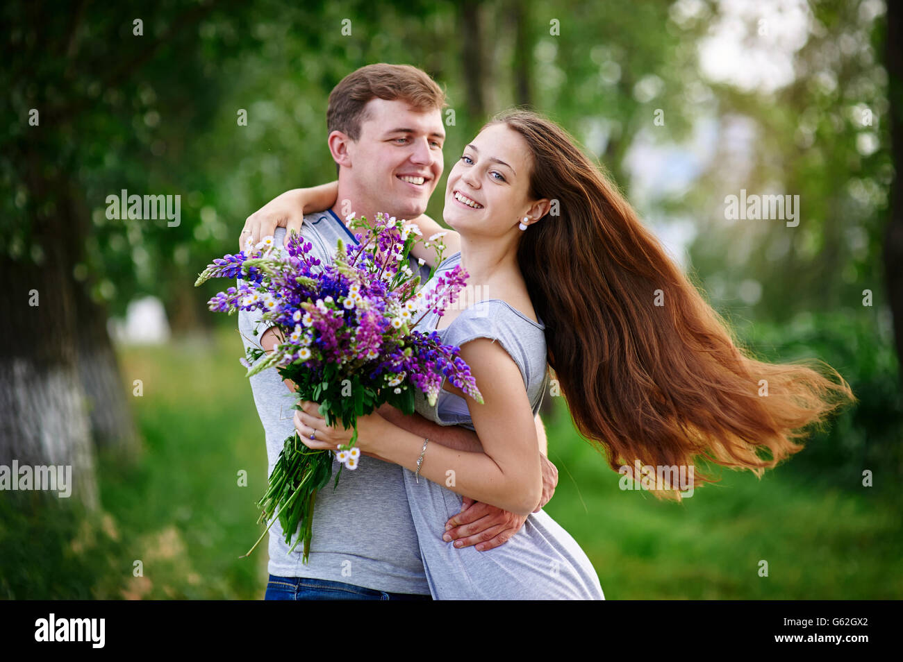 beautiful woman with long hair and a happy man hugging in field Stock Photo