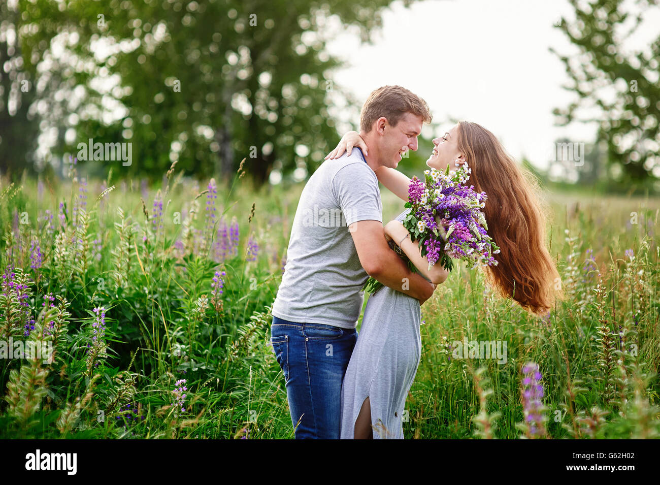 beautiful woman with long hair and a happy man hugging in field Stock Photo