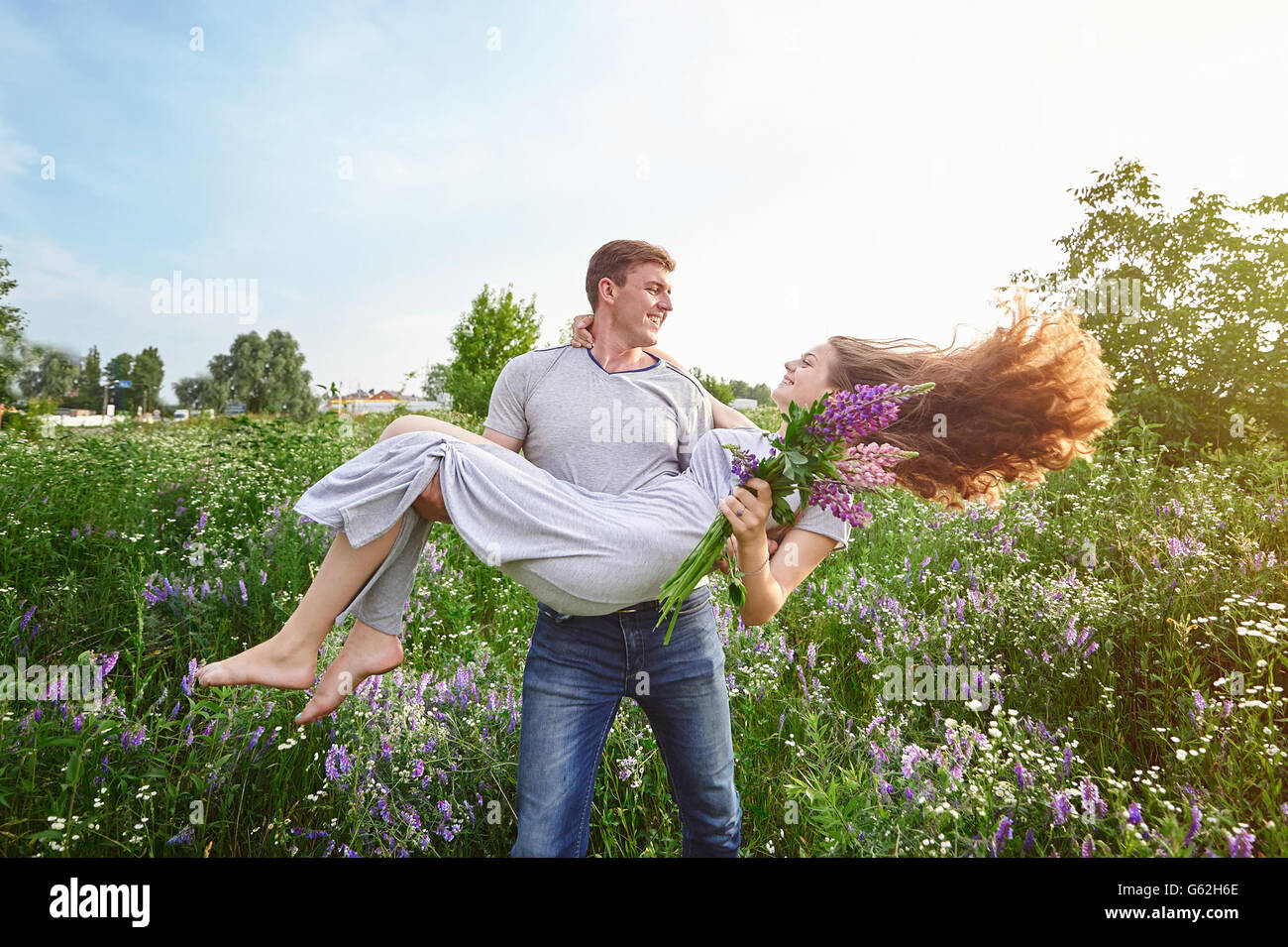 Happy love man holding a woman on his arms in field Stock Photo