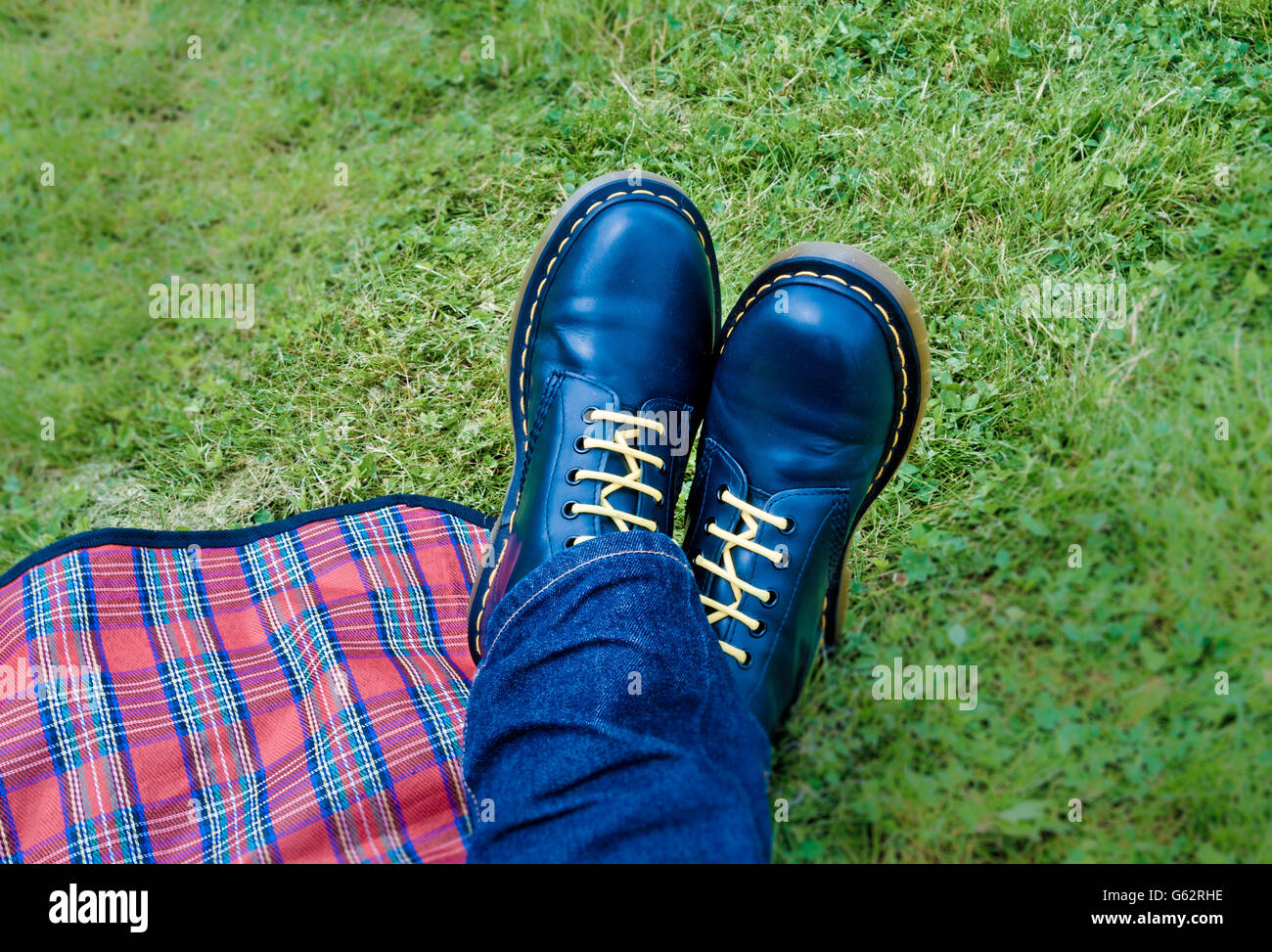 Feet with blue Dr Marten's Boots and red plaid picnic blanket on grass Stock Photo