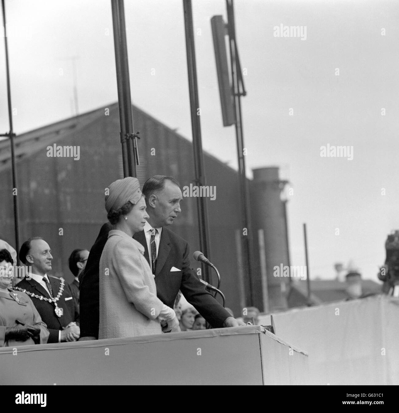 Wearing a wool coat of deep turquoise and a matching suede hat, The Queen presses the button to launch the new Cunard liner after revealing the names as Queen Elizabeth II at John Brown's Yard, Clydebank, Scotland. The name of the 58,000-ton liner was kept secret until the launching. The 25,500,000 vessel is destined to give Britain a world lead with the most advanced passenger liner ever built. Stock Photo