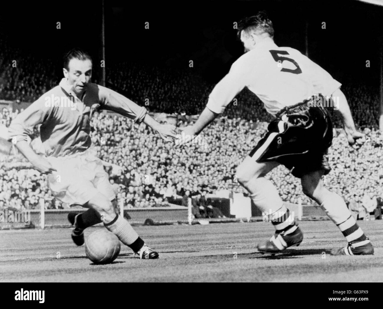 Outside right Stanley Matthews cooly steers the ball past Bolton's centre half M Barass in the thrilling FA Cup final at Empire Stadium, Wembley. Matthews put over the centre from which Bill Perry scored the fourth and winning goal to give Blackpool the Cup and Stanley his coveted Cup winner's medal. Stock Photo