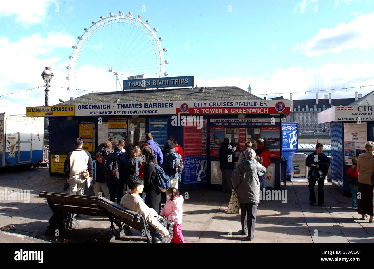 Tourists queue at kiosks in front of the London Eye for tickets for boat cruises down the River Thames. Stock Photo