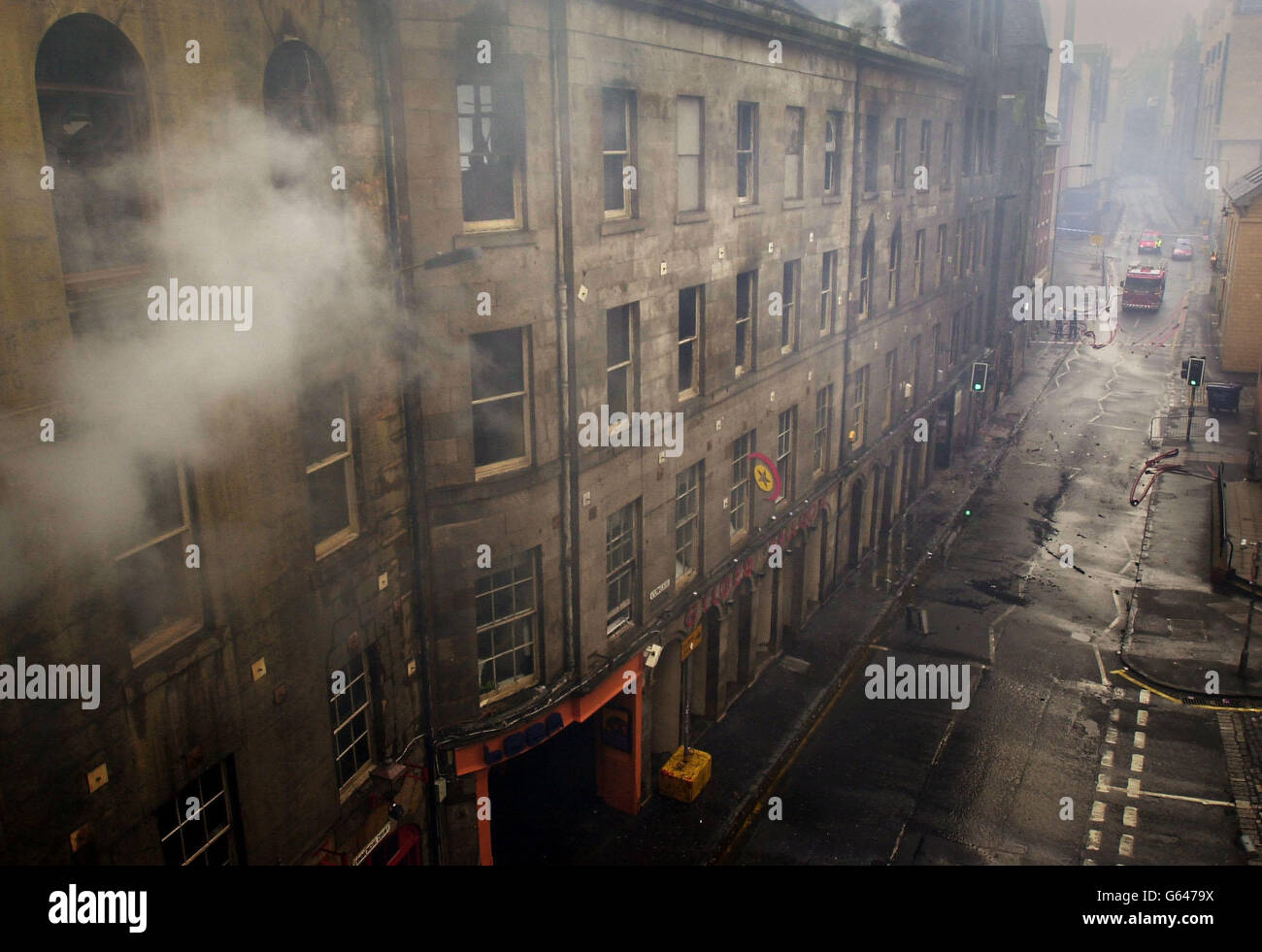 A firefighter trains his hose on buildings in Edinburgh's Cowgate, with Edinburgh University in the background, after a fire which began the night before. Firefighters were still battling to contain the blaze which has devastated part of the city's historic Old Town, *..causing millions of pounds worth of damage, more than 12 hours since it first broke out in a nightclub there. Stock Photo