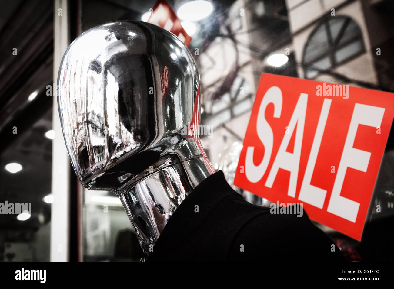 Faceless silver mannequin head dark close-up. Red sale sign Stock Photo