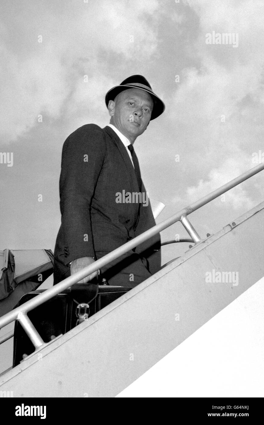 Yul Brynner, the Hollywood actor with the smooth scalp, wears a hat as he boards an aircraft at Heathrow Airport, London. Stock Photo