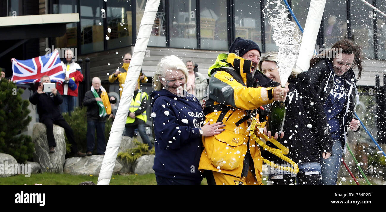 Gerry Hughes opens a bottle of Champagne with his wife Kathleen (left) and daughters Ashley (2nd right) and Nicola (right), after arriving at Troon Marina in Scotland to make him the first deaf person to have sailed single-handed around. Stock Photo