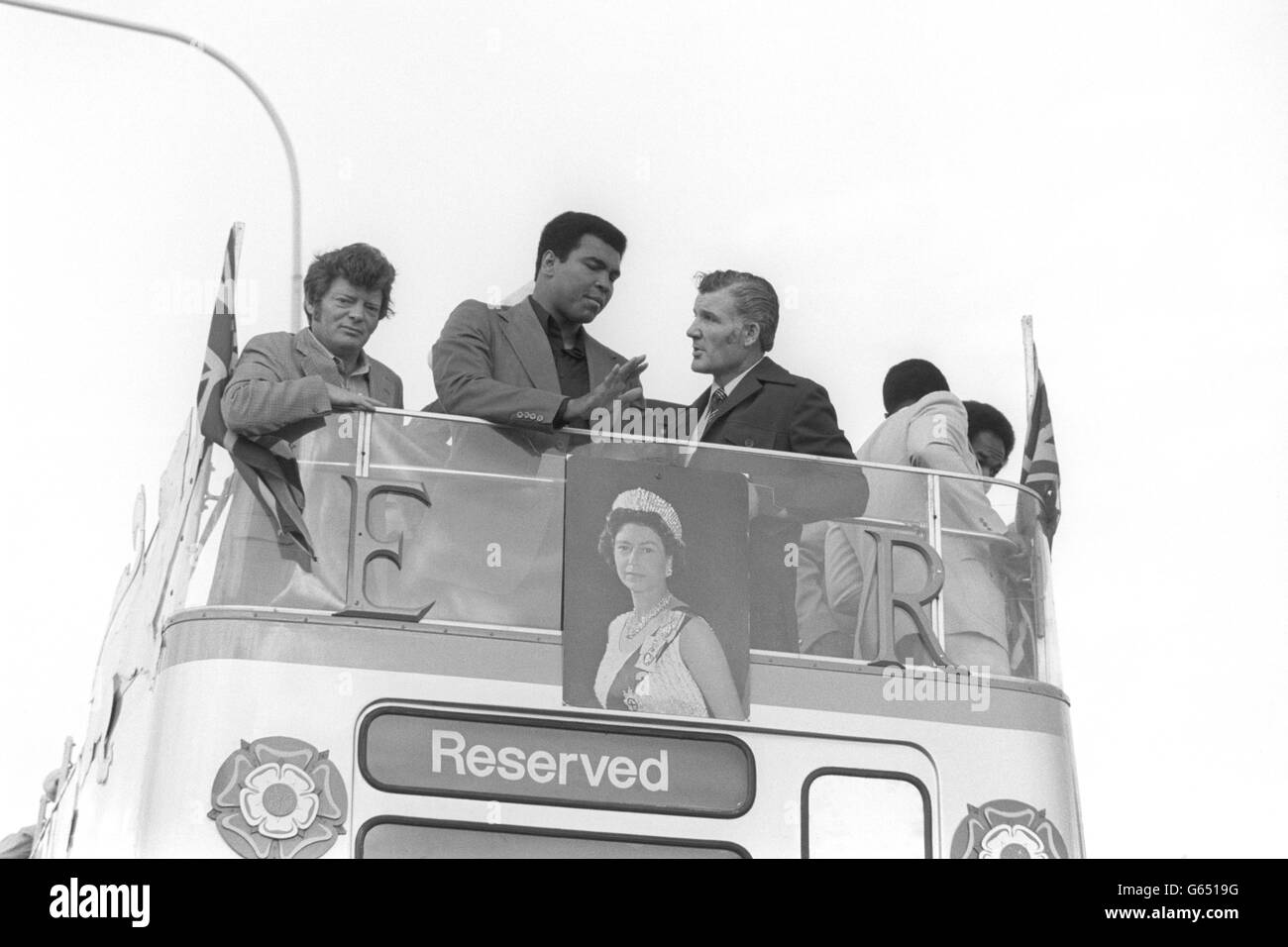 White rose in his hand, boxer Muhammed Ali, acknowledges the cheering crowd from an open-topped double-decker bus, which is decorated with a Union Jack and a poster of the Queen. The Tyneside crowd gave him a warm welcome as he left the southern end of the Tyne Tunnel. He drove seven miles to a stadium hwere South Shields carnival was being held. Ali is on the third day of his trip to the region, where he is visiting boys' boxing clubs across Tyneside to help raise money for them. Stock Photo