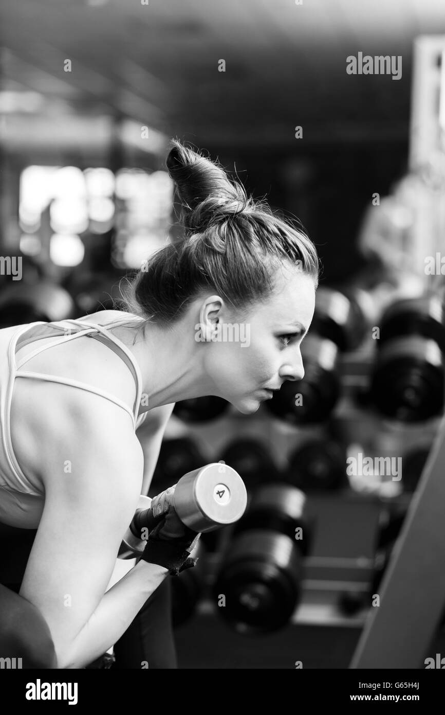 Young confident woman doing biceps curl exercise with dumbbells in fitness center. Slim girl training in the gym with dumbbells. Stock Photo