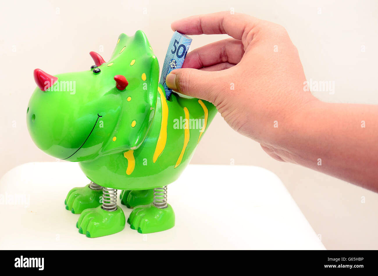 Hand putting money in Dino piggy bank, with  Rupiah currency Stock Photo