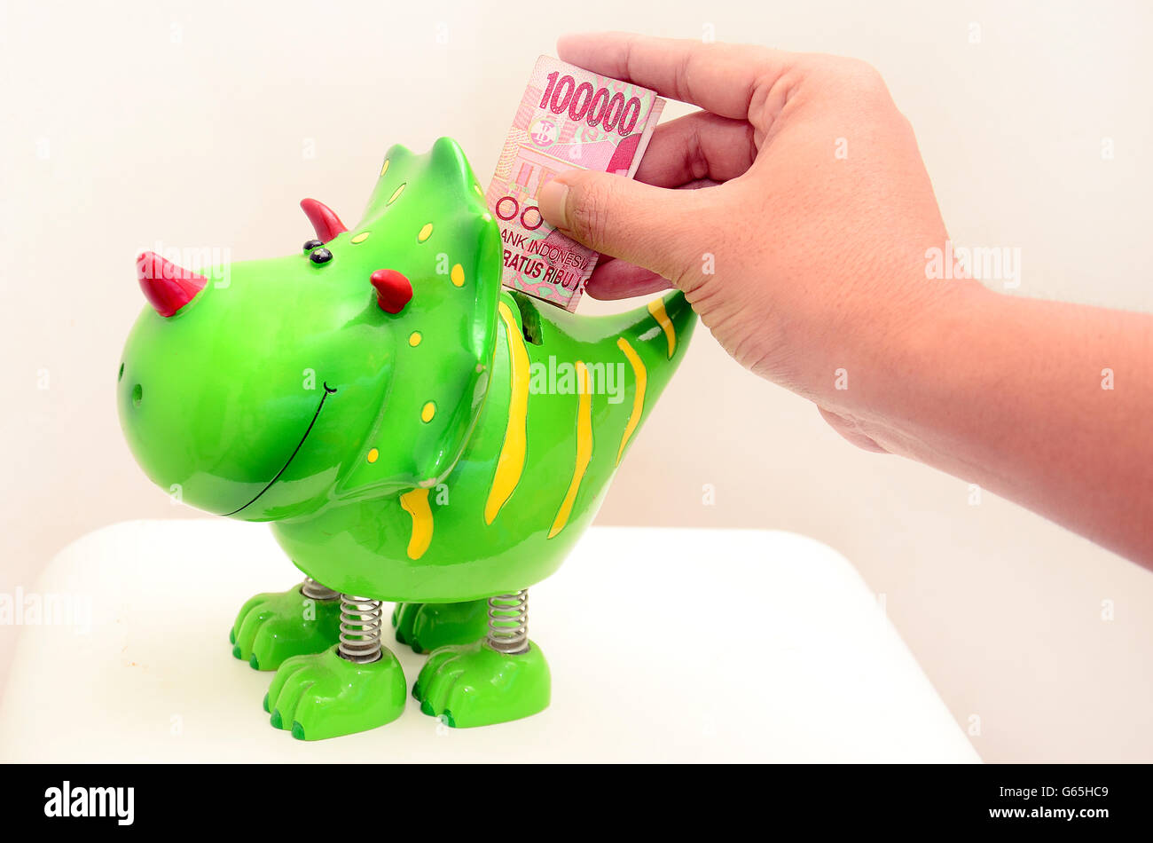 Hand putting money in Dino piggy bank, with  Rupiah currency Stock Photo