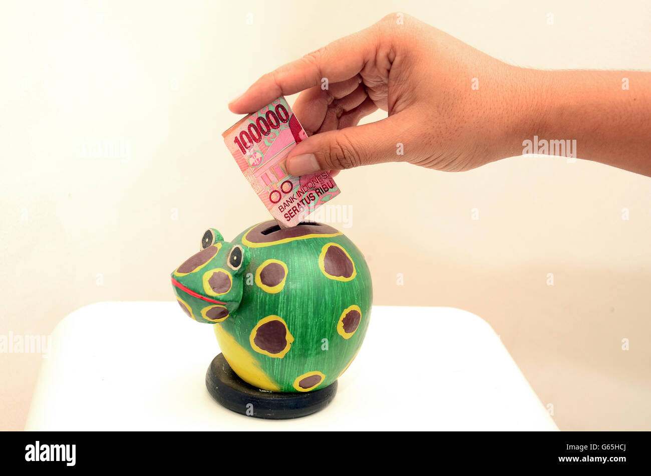 Hand putting money in frog piggy bank, with  Rupiah currency Stock Photo