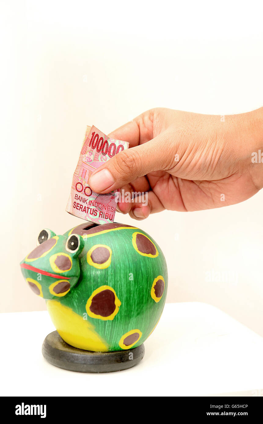 Hand putting money in frog piggy bank, with  Rupiah currency Stock Photo