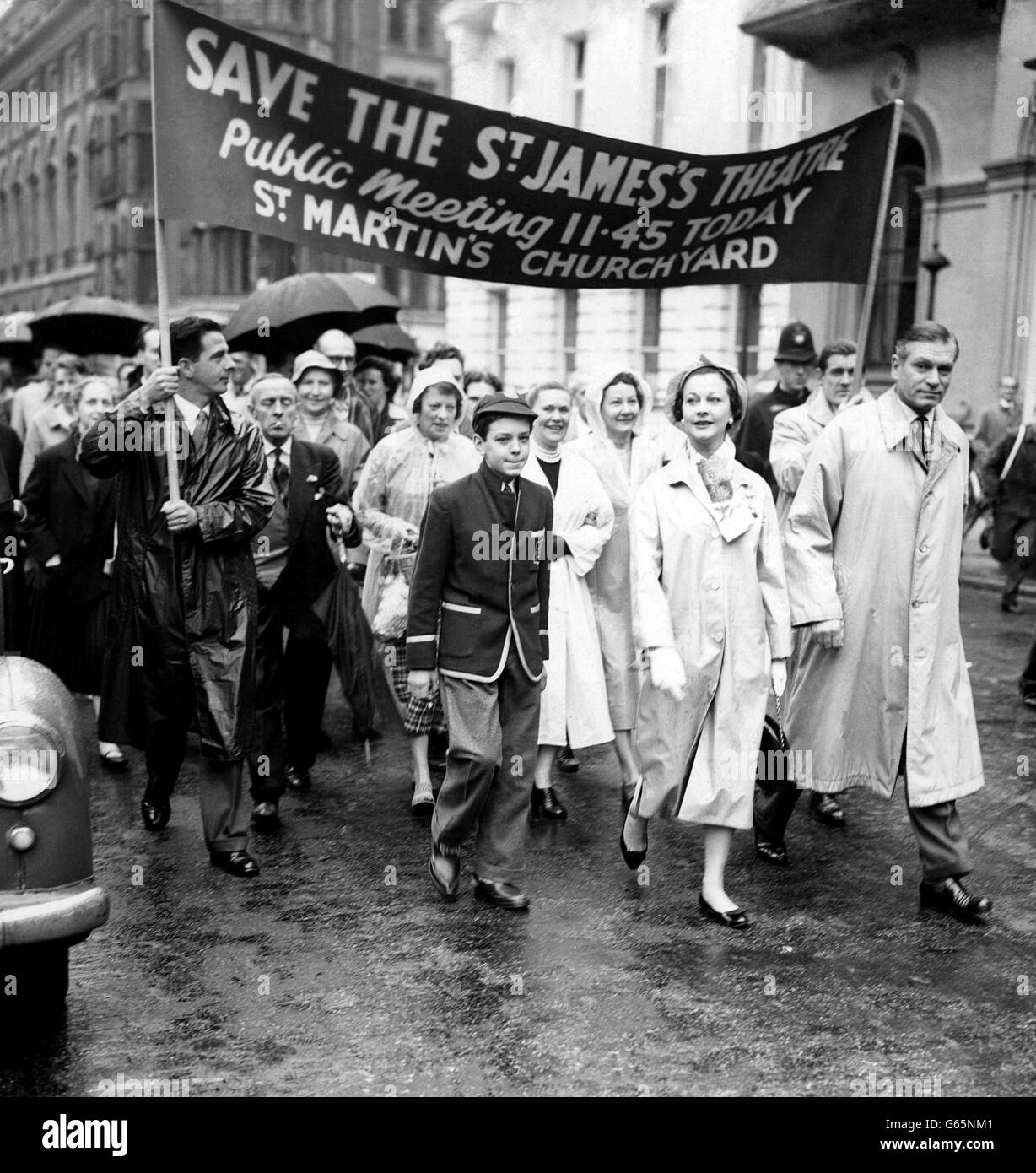 Stepping out in front of a banner are actor Sir Laurence Olivier and his actress wife Vivien Leigh. They are seen in St. James's Square, London, as they headed a procession through the rain from the St James's Theatre to the courtyard of St Martin-in-the-Fields Church, Trafalgar Square, where there were to be speeches. The public march and meeting had been called by British Actors' Equity to protest against the closing of the St James's Theatre and to focus attention on the continued closing of theatres throughout Britain. Stock Photo