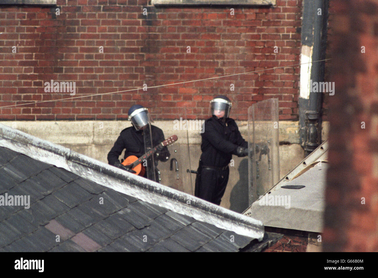 An officer in riot gear strums a guitar left behind by a prisoner following the siege at Strangeways prison. Stock Photo