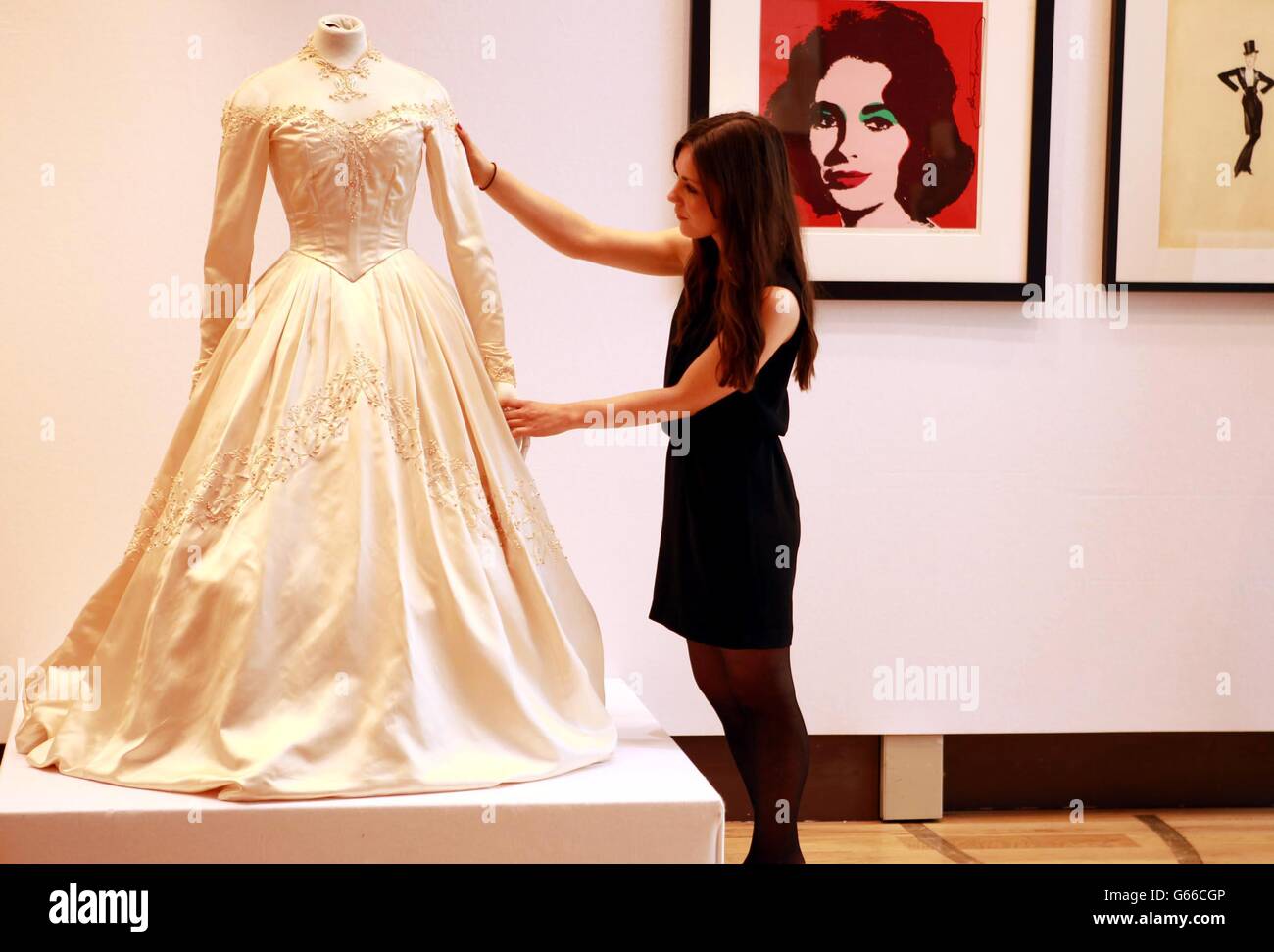 A Christie's staff member adjusts a wedding dress worn by Elizabeth Taylor, for her first wedding to Conrad Nicky Hilton in 1950 which has an estimated sale price of £30.000-£50.000 during a photocall for the 120 years of Pop Culture sale at Christie's in London. Stock Photo